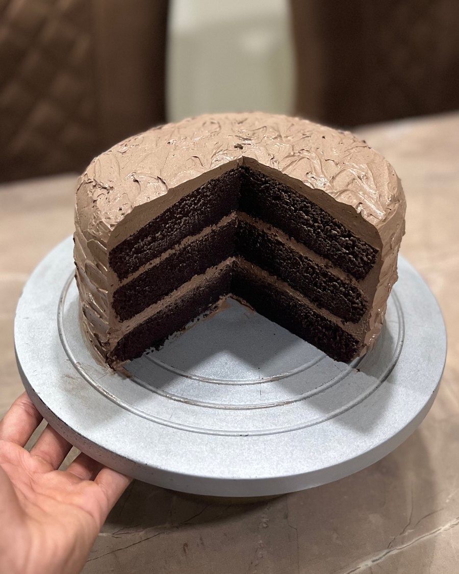 A hand steadying a cut chocolate layer cake on its stand