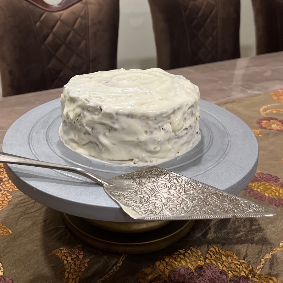 A cream cheese frosted cake on a stand, cake server beside it