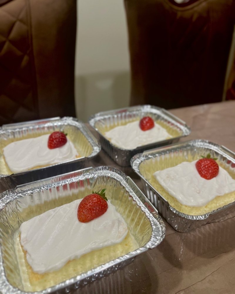 Tres leches in trays, topped with cream and a strawberry